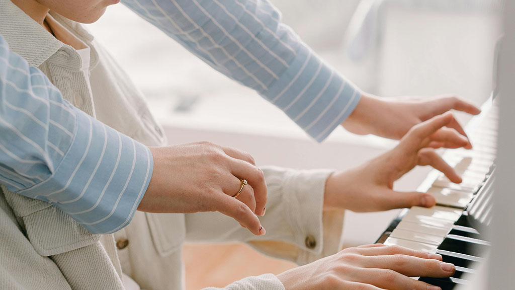 A parent helping their child playing the piano