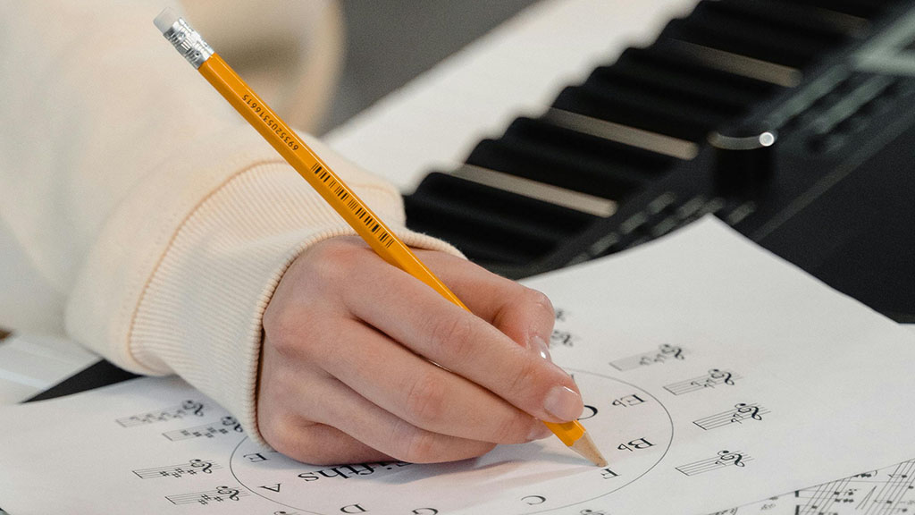 A Hand holding a pencil working on music theory worksheets